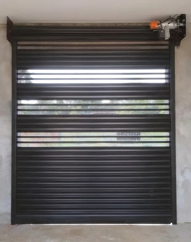 Porta de enrolar preta combinando faixas de chapa lisa e transvision, com o motor e a testeira à vista